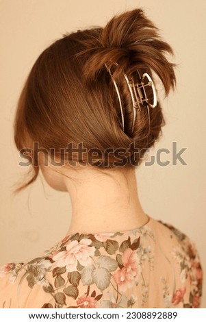A young, strawberry blonde woman with her back to the camera to showcase an elegant, gold, metal claw clip which holds her hair up in an elegant style. 