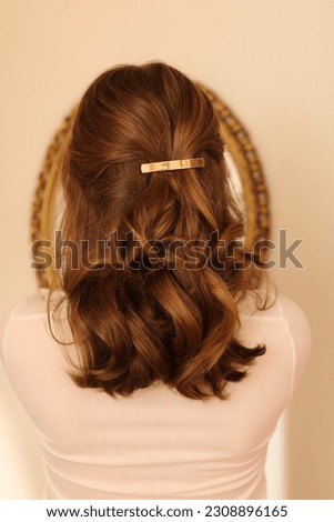 A young, blonde woman stands with her back to camera to showcase a gold, metal French barrette hair clip which holds her hair half-up in an elegant hairstyle.  Royalty-Free Stock Photo #2308896165