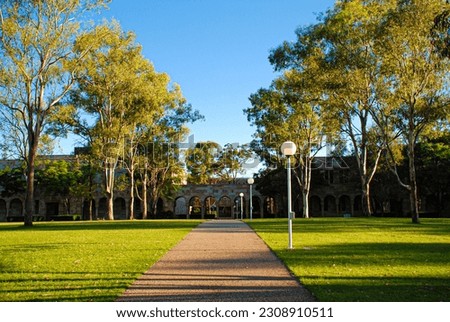 Footpath walkway leading to university campus with trees on both sides and green grass lawn field with lamp posts on one side of the footpath walkway Royalty-Free Stock Photo #2308910511