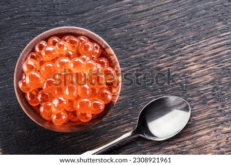 Red caviar in the bowl with silver spoon on a wooden background. Top view.