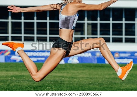 close-up female athlete jumping triple jump in summer athletics championships on background green field Royalty-Free Stock Photo #2308936667