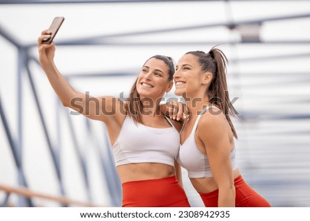 Happy sporty twin sisters taking a picture with cell phone