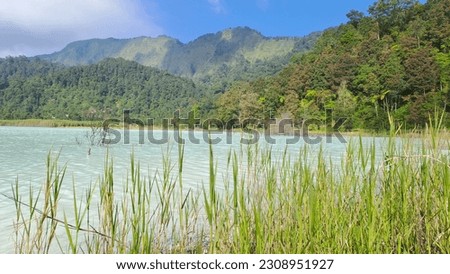 Beautiful lake embcraced by towering mountains and abundant greenery. The tranquil, blue-whitish waters reflect the breathtaking scenery. Captured at Talaga Bodas, Garut, Indonesia