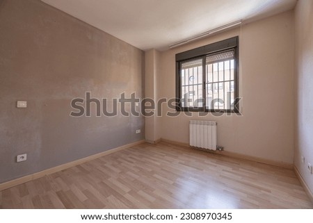 An empty room with dirty brown walls, a brown aluminum window with bars and a light wooden floor