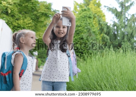 Little girls, sisters use a mobile phone on the way to school