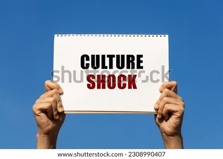 Culture shock text on notebook paper held by 2 hands with isolated blue sky background. This message can be used as business concept about culture shock.