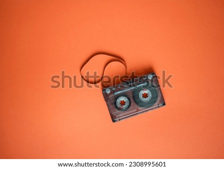 Audio cassette with stretched tape on orange background, top view.