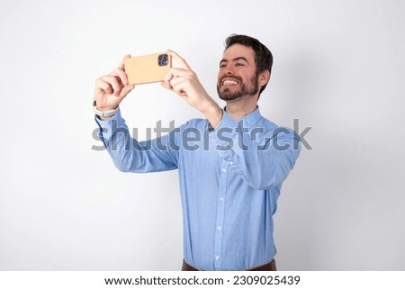 handsome businessman wearing blue shirt over white studio background taking a selfie to post it on social media or having a video call with friends.