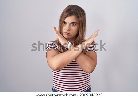 Young hispanic woman standing over isolated background rejection expression crossing arms doing negative sign, angry face 