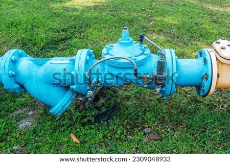 Close-Up View of a Gate Valve in a Piping System Amidst a Lush Grassy Field - Efficient Fluid Control Solutions