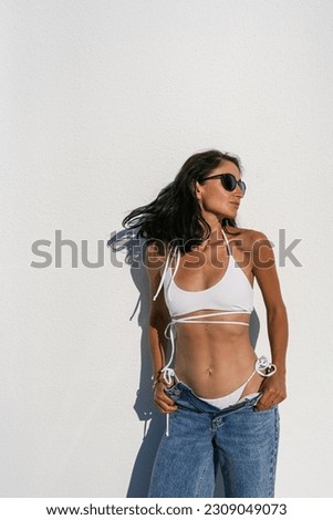 brunette girl in glasses in a white swimsuit and blue jeans agai