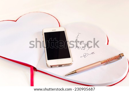I love you note. Smartphone and Valentine love message in opened red heart shaped paper notebook. 
