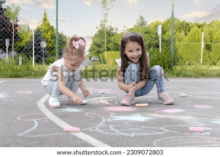 Two little sisters are drawing on the children's playground. Happy childhood