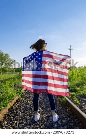 Rear view of woman holding an American flag outdoors. Young woman with american flag. USA Independence Day Celebration. 