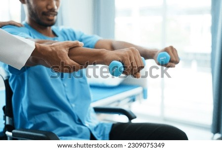 physiotherapist helping male patient in wheelchair exercise with dumbbells.