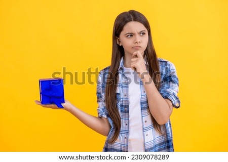 pondering teen girl with shopping box isolated on yellow. teen girl shopping with present in studio. teen girl holding shopping box on background. teen girl after successful shopping