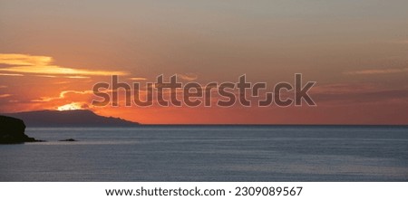 Sunset over Greek island, Cyclades, Greece. Sun goes to sleep behind hill silhouette colors the sky orange, yellow. Calm blue Aegean sea. Banner