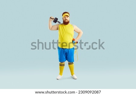 Funny serious fat male athlete with sports equipment on pastel light blue background. Full length of man in sportswear holding dumbbells and skipping rope and looking at camera with serious expression