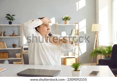 Oh god it's too hot today. Fat woman suffering from unbearable heat, sitting at work desk at home, wiping sweat off her forehead, and refreshing herself with paper fan. High summer temperature concept Royalty-Free Stock Photo #2309092155