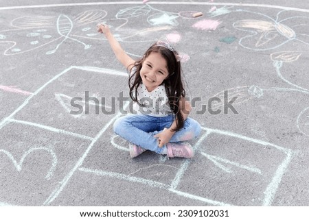 Little preschool girl painting  with colorful chalks on ground . Positive happy toddler child drawing and creating pictures. Creative outdoors activity in summer