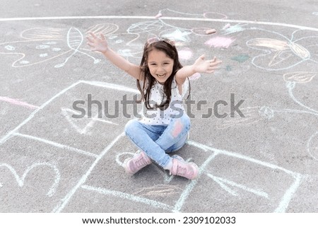 Little preschool girl painting  with colorful chalks on ground . Positive happy toddler child drawing and creating pictures. Creative outdoors activity in summer