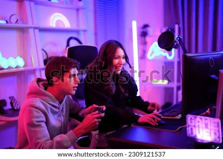 Caucasian young streamer boy and Asian influencer girl playing video game online while broadcast live on their channel for review technology gadget such as monitor, keyboard and joystick together