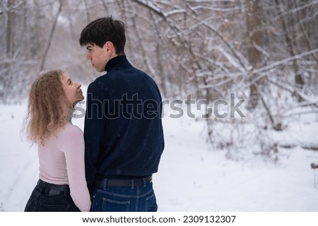 A young couple walks in the park in winter without jackets. Boy and girl hugging on the street. 