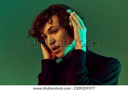 Man portrait in headphones listening to music, dancing and singing, DJ happiness and smile laughter, hipster teen lifestyle, portrait green background mixed neon light, copy space