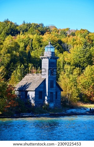 Lighthouse on Lake Superior shore with boarded up windows and green forest beyond