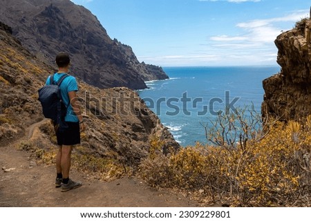 Backpack man on hiking trail from Afur to Taganana with scenic view of Atlantic Ocean coastline and Anaga mountain range, Tenerife, Canary Islands, Spain, Europe. Looking at Cabezo el Tablero crag Royalty-Free Stock Photo #2309229801
