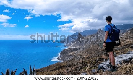 Backpack man with scenic view of Atlantic Ocean coastline and Anaga mountain range on Tenerife, Canary Islands, Spain, Europe. Looking at Roque de las Animas crag. Hiking trail from Afur to Taganana Royalty-Free Stock Photo #2309229823