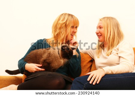 best friends at home - 2 happy girlfriends sitting on a sofa talking and laughing while a cat sits on a lap and listens