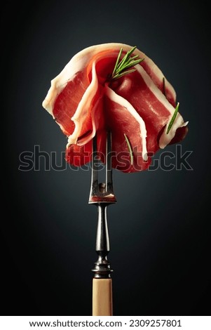 Sliced prosciutto with rosemary on a fork. Royalty-Free Stock Photo #2309257801