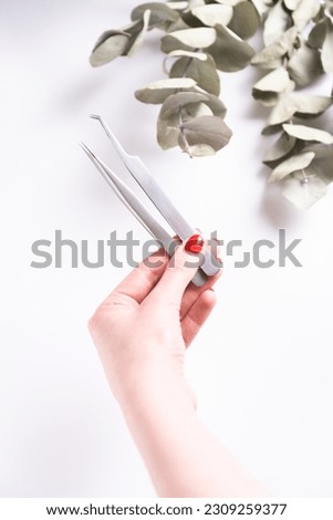Woman hand holding pair of metal tweezers for eyelash extension  Royalty-Free Stock Photo #2309259377