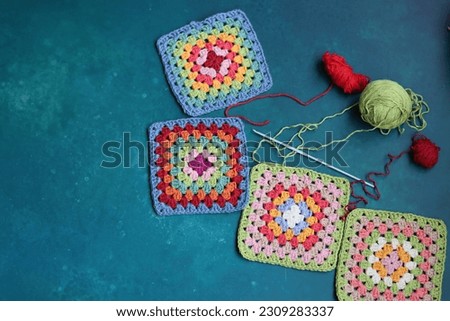 Multicolored Afghan squares, cotton yarn and crochet hook on vibrant blue background with copy space. Hobby and leisure concept. Arts and crafts supplies.  