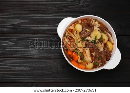 Pot of delicious vegetable soup with meat, noodles and ingredients on black wooden table, top view. Space for text