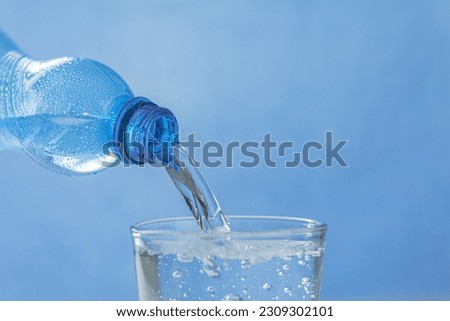 Cool water flows from the bottle into the glass. Pouring water from a bottle into a glass on a blue background. Place for text