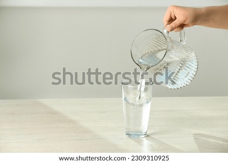 Woman pouring water from jug into glass on white table indoors, closeup. Space for text Royalty-Free Stock Photo #2309310925