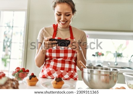 Young beautiful hispanic woman smiling confident make photo by smartphone to cupcake at the kitchen
