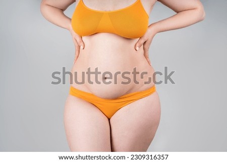 Fat woman in orange underwear on gray background, overweight female body, body positive concept