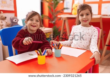 Adorable girls preschool students sitting on table drawing on paper at kindergarten Royalty-Free Stock Photo #2309321265