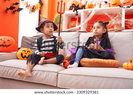 Adorable boy and girl having halloween party sitting on sofa at home