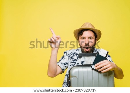 Surprised mid adult man looking excited while pointing up with his finger and ready to travel on summer vacations in front of a yellow background