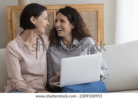 Cheerful positive middle aged mother and happy adult daughter woman using modern technology, software, application on laptop computer for shopping, Internet communication, laughing