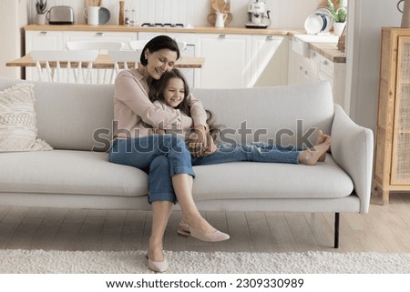 Cheerful loving grandmother and cute grand kid girl resting on sofa. Grandma hugging preschooler child on home couch, laughing, smiling, enjoying family leisure time