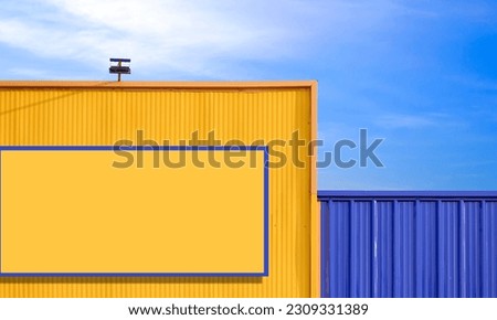 Colorful yellow and blue corrugated metal building wall with blank advertising billboard and spotlight against blue sky background Royalty-Free Stock Photo #2309331389