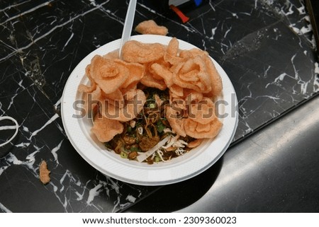 Indonesian food, chicken porridge with topping, chicken pieces, peanuts, green onions, fried onions and crackers. The porridge is filled with chicken stock and sweet soy sauce.