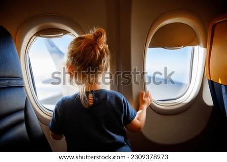 Adorable little girl traveling by an airplane. Child sitting by aircraft window and looking outside. Traveling with kids abroad. Family on summer vacations. Royalty-Free Stock Photo #2309378973