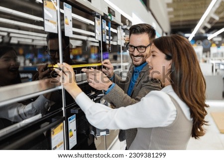 Beautiful and happy middle age couple buying consumer tech products in modern home appliances store. They are choosing electrical cooker and oven. People and consumerism concept. Royalty-Free Stock Photo #2309381299