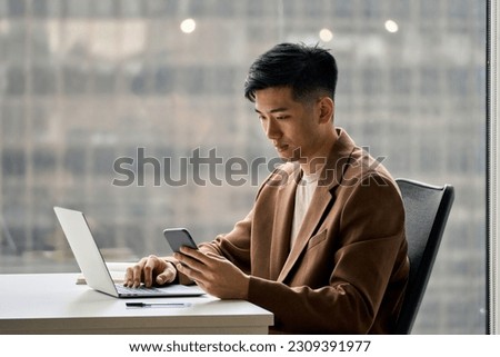 Young busy smart serious Asian Japanese business man executive holding cellphone device using mobile cell phone looking at smartphone working in corporate office with laptop computer technology. Royalty-Free Stock Photo #2309391977